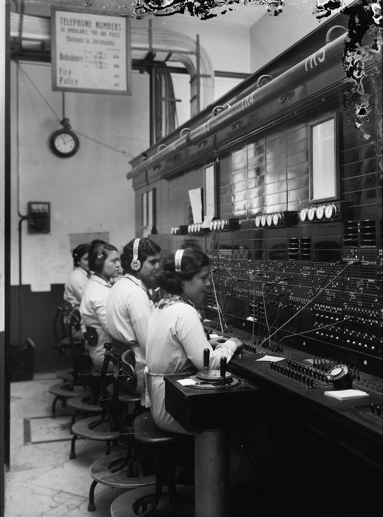 Vier telefonistes aan een schakelbord met stekkers en koorden